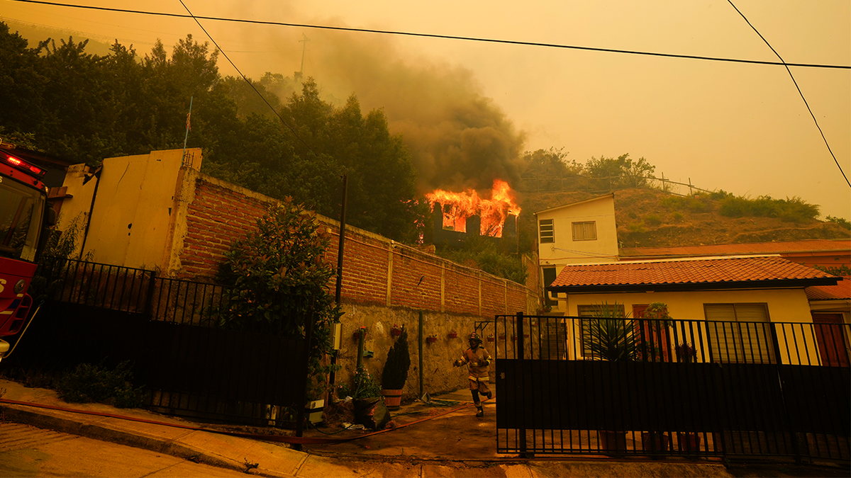 Ein Feuerwehrmann rennt durch einen Vorgarten, während ein Gebäude in Flammen aufgeht