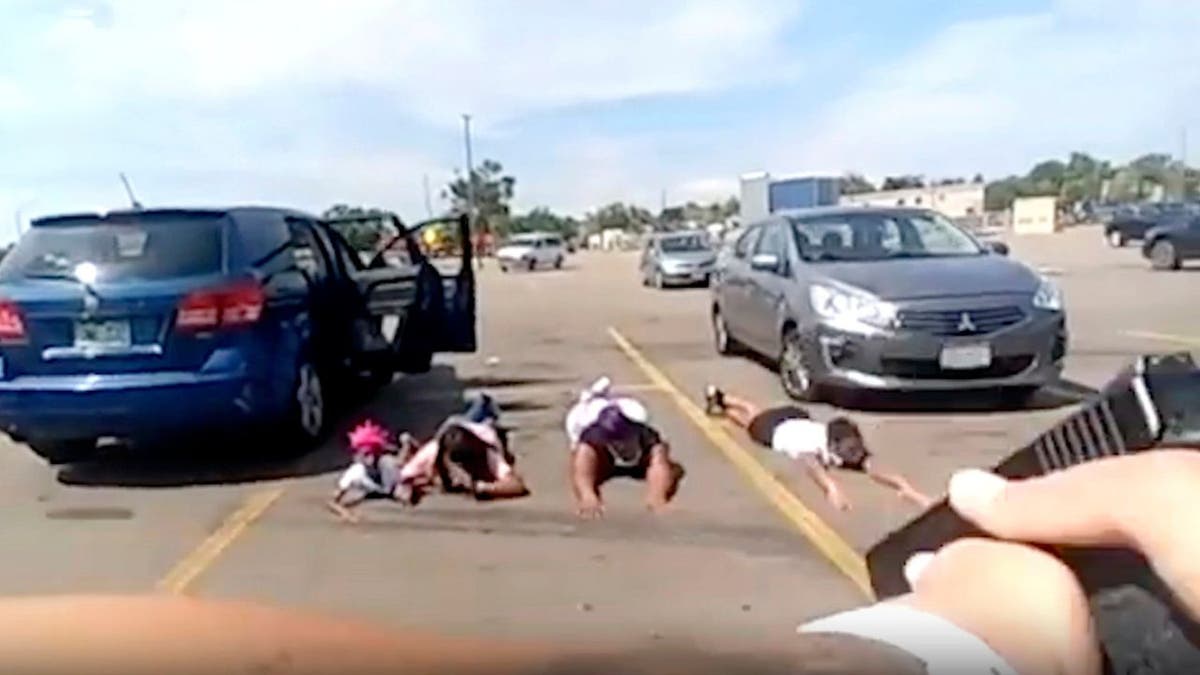 Bodycam-Screenshot eines Polizisten, der seine Waffe auf vier junge Mädchen richtet, die mit dem Gesicht nach unten auf einem Parkplatz liegen 