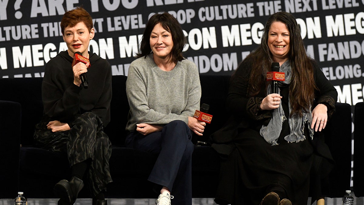 Rose McGowan in Schwarz sitzt neben Shannen Doherty in einem grauen Pullover in der Mitte, neben Holly Marie Combs in Schwarz