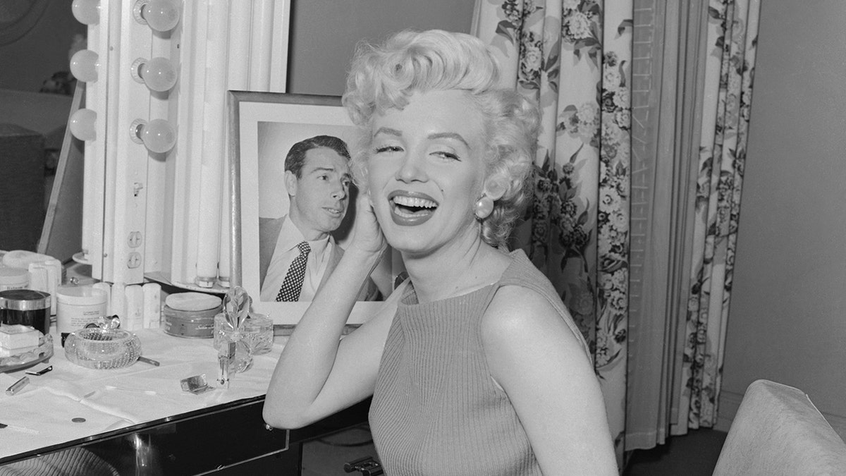 Marilyn Monroe lächelt neben einem Porträt von Joe DiMaggio