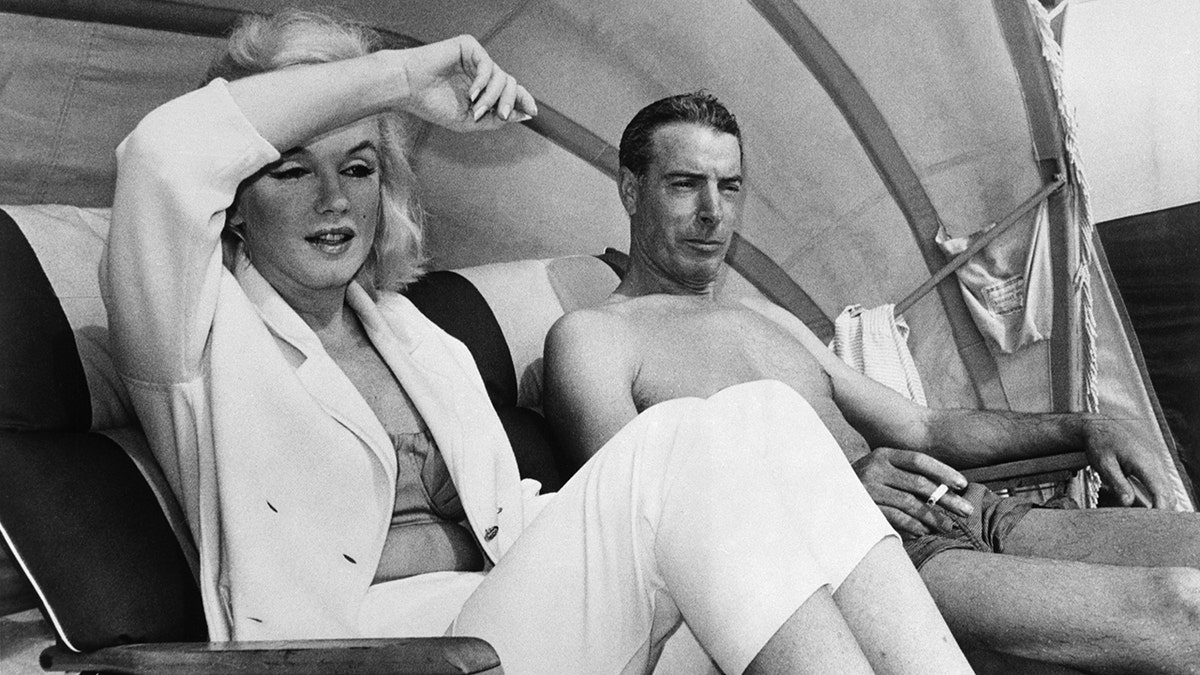 Marilyn Monroe und Joe DiMaggio sitzen zusammen am Strand