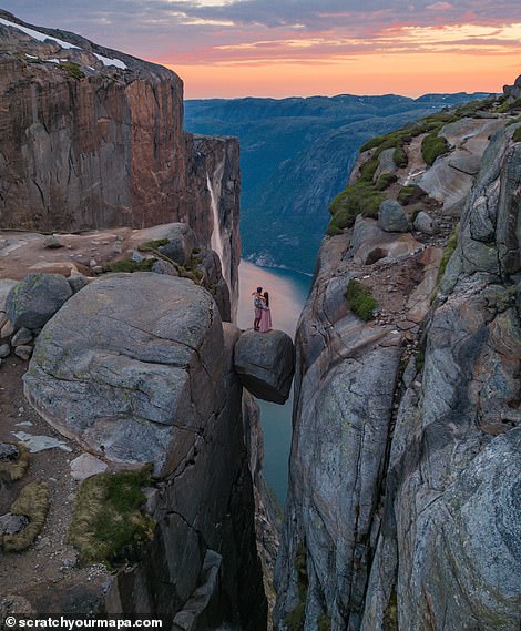 Danni und Fede stehen auf dem Kjeragbolten, einem Felsbrocken, der in einer Felsspalte 984 m (3.228 Fuß) über dem Meeresspiegel auf dem Kjerag-Berg im Lysefjord in Norwegen eingeklemmt ist.  Das beliebte Touristenziel kann ohne Wanderausrüstung erreicht werden