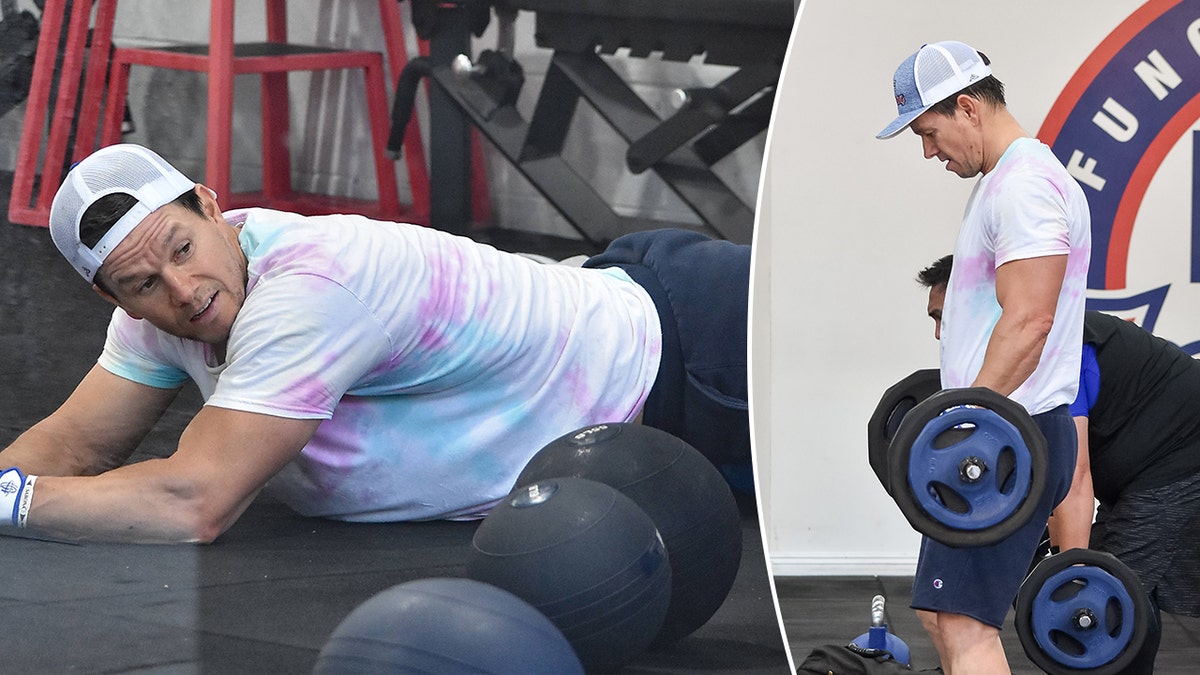 Mark Wahlberg auf dem Boden einer Turnhalle mit Gewichtsbällen beim Heben von Gewichten