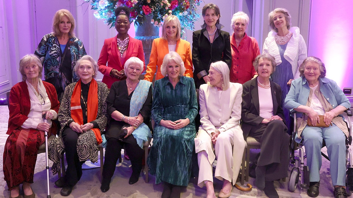 Königin Camilla in einem dunkelgrünen Kleid ist von Damen umgeben, darunter Judi Dench zu ihrer direkten Linken