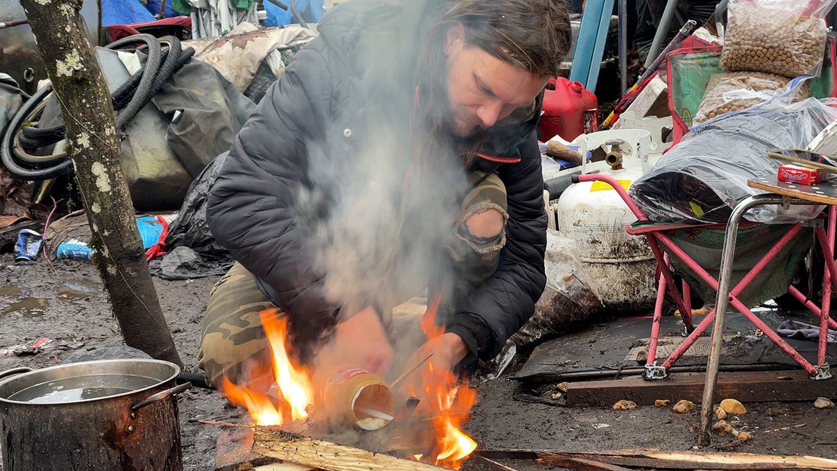 Ein Mann versucht, in einem Obdachlosenlager ein kleines Lagerfeuer anzuzünden