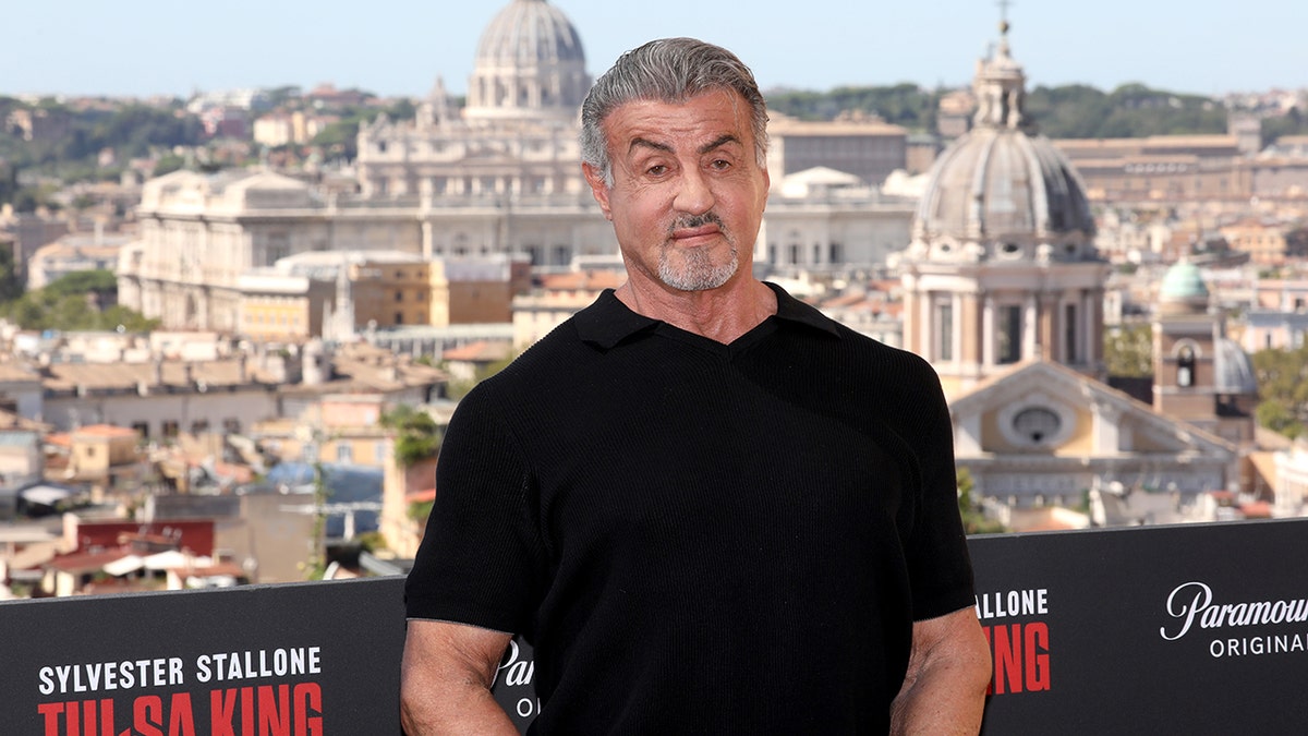 Sylvester Stallone in einem schwarzen T-Shirt mit der Kulisse Roms im Rücken