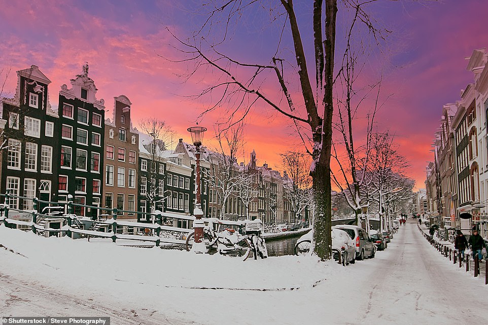 Pictured is the city of Amsterdam covered in thick snow beneath a glowing purple sky. 'The city looks like a Christmas card when it’s dusted in snowflakes – making for a wildly romantic backdrop to any visit,' Iamsterdam says, billing the Dutch capital a 'perfect' winter destination. There are plenty of winter activities, the travel website notes, and visitors may even get the chance to ice skate on frozen winter canals if temperatures drop low enough