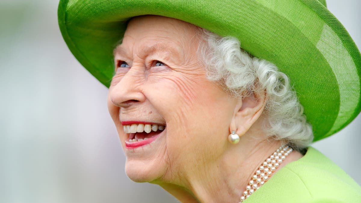 Königin Elizabeth lächelt breit, während sie einen leuchtend grünen Mantel mit passendem Hut trägt.