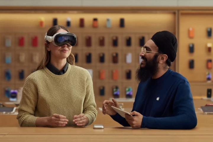 Ein Apple-Mitarbeiter zeigt einer Person in einem Apple Store, wie man ein Vision Pro-Headset verwendet.