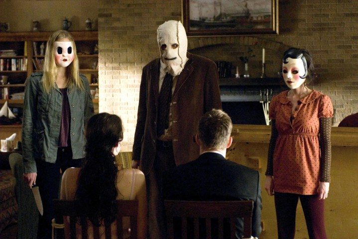 In „The Strangers“ stehen drei maskierte Figuren vor einem Paar.