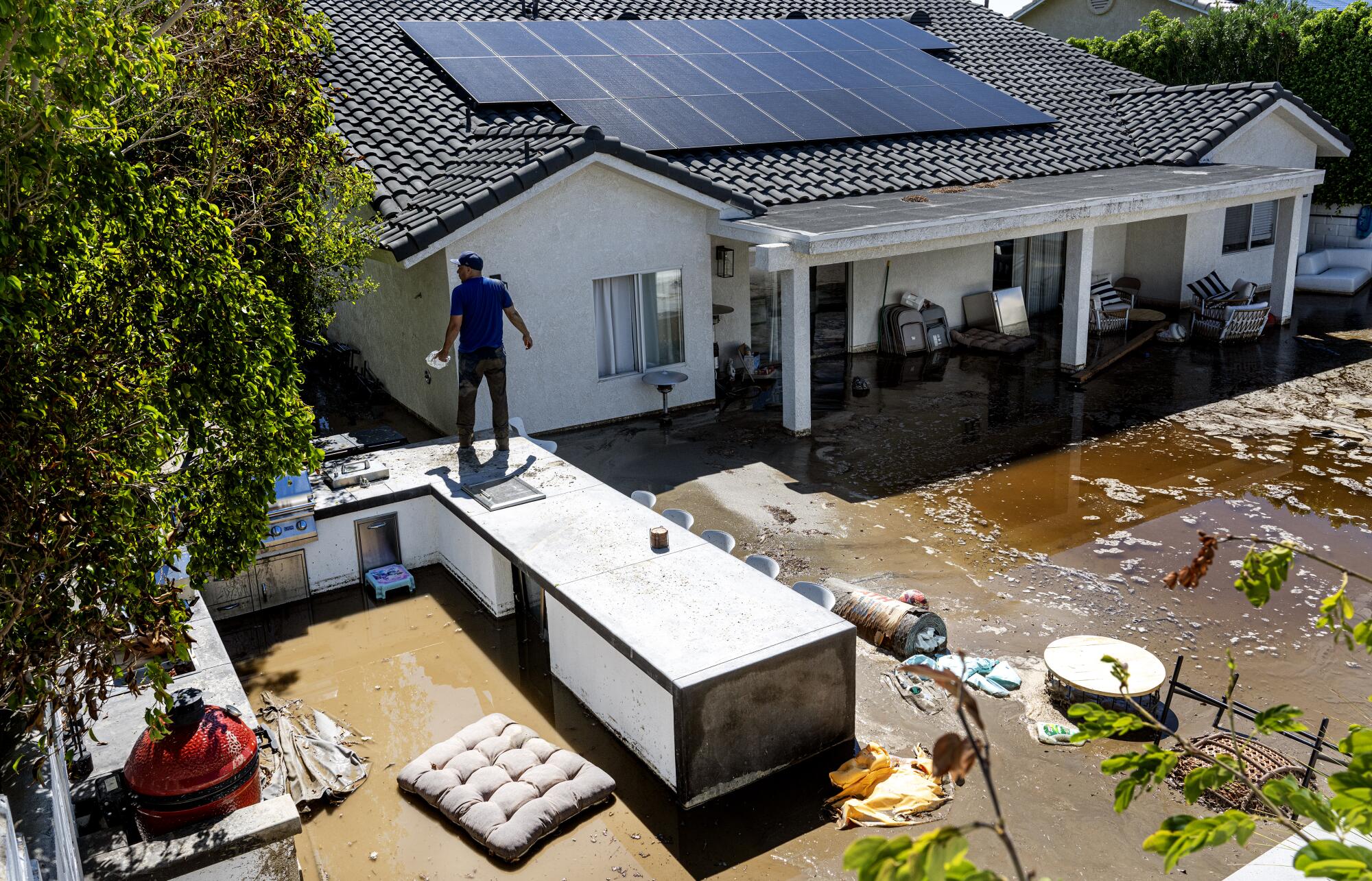Ein Mann steht auf einem Außengrill vor einem überschwemmten Haus.
