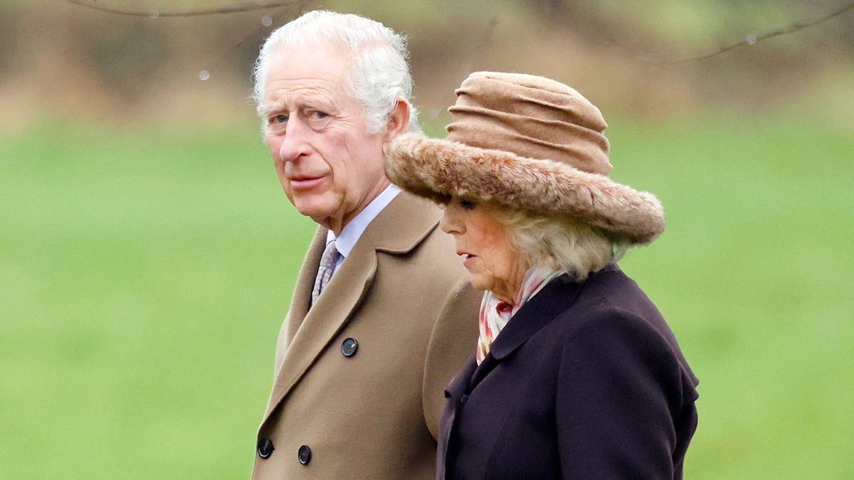 König Charles geht in einem hellbraunen Mantel neben seiner Frau Königin Camilla in einem dunklen Mantel und einem hellbraunen Hut