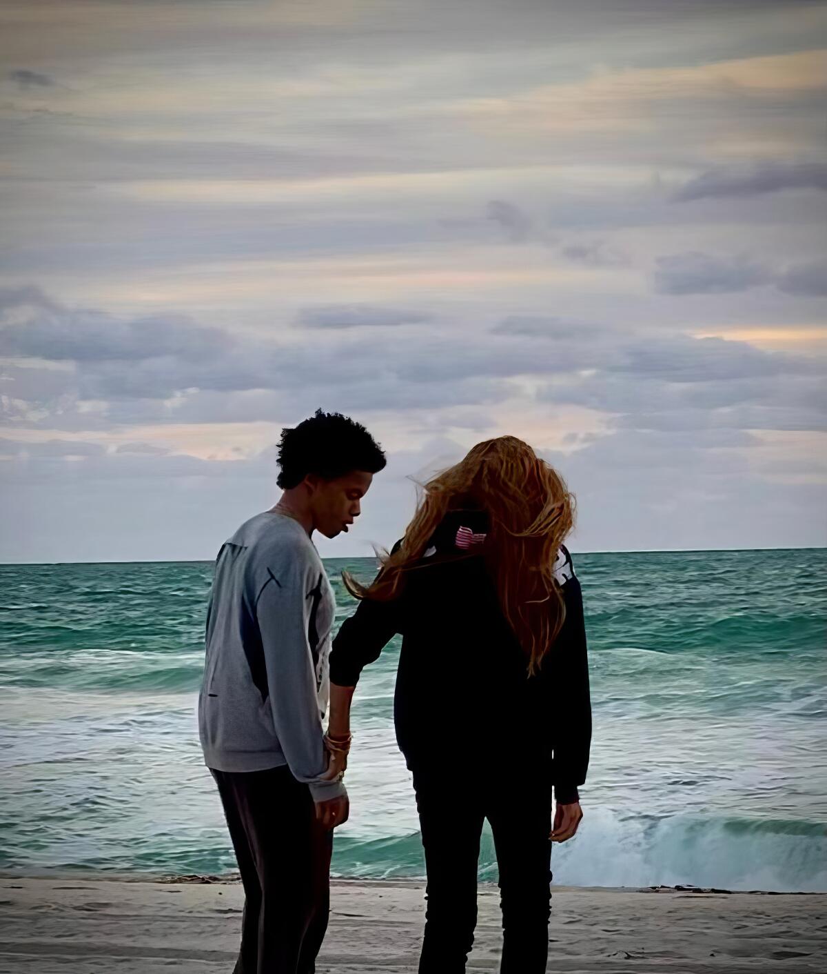 Zwei Menschen gehen am Strand spazieren und schauen auf die Wellen des Ozeans.