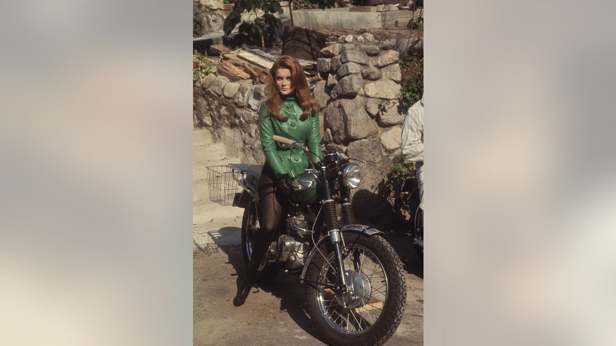 Ann-Margret trägt einen grünen Pullover und schwarze Strümpfe auf einem Motorrad