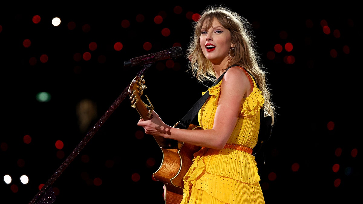Taylor Swift spielt während ihrer Eras-Tour in einem leuchtend gelben Kleid Gitarre auf der Bühne