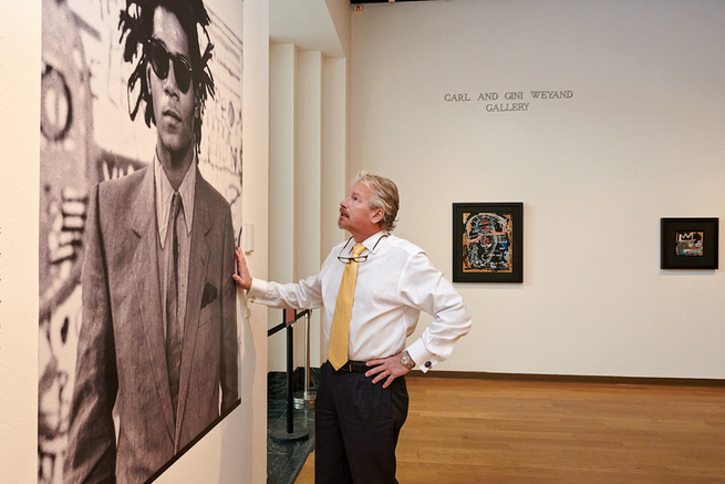 Ein Mann betrachtet ein großes Porträt von Basquiat in der Museumsgalerie, im Hintergrund hängen zwei Gemälde.