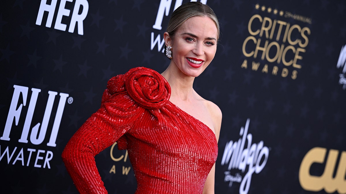 Emily Blunt in einem glitzernden roten Kleid mit Rosen auf der Schulter auf dem Teppich der Critics Choice Awards