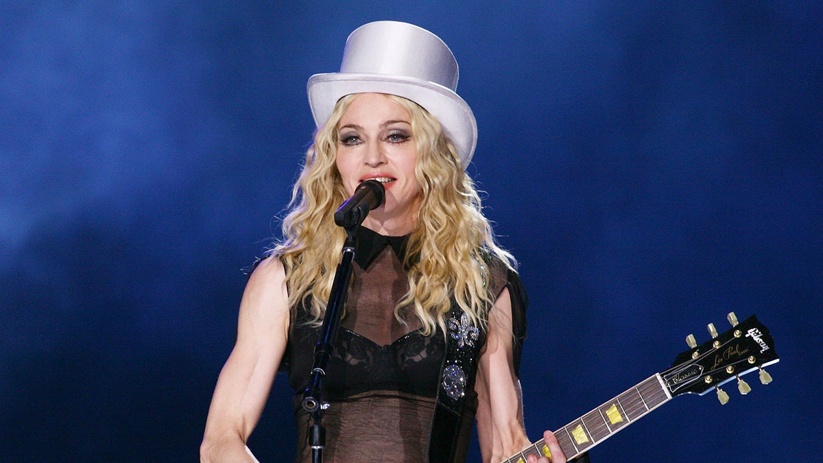 Madonna trägt bei Konzert einen weißen Zylinder und spielt Gitarre