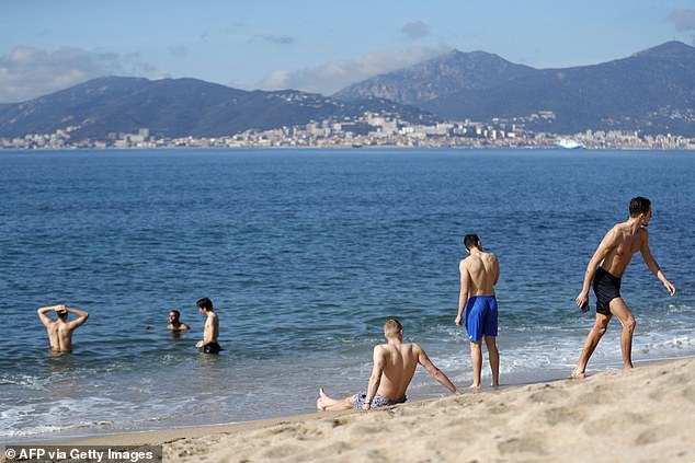 Männer baden an einem warmen Wochenende im 14 °C warmen Meer, mit den Sanguinaires-Inseln im Hintergrund, auf der französischen Mittelmeerinsel Korsika, in Porticcio, 18. Februar 2024