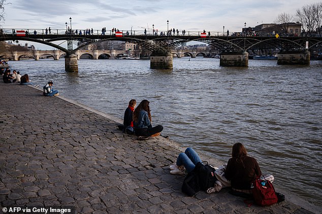 Am 15. Februar 2024 sitzen Menschen am Ufer der Seine und genießen das warme Wetter vor der Pont des Arts in Paris
