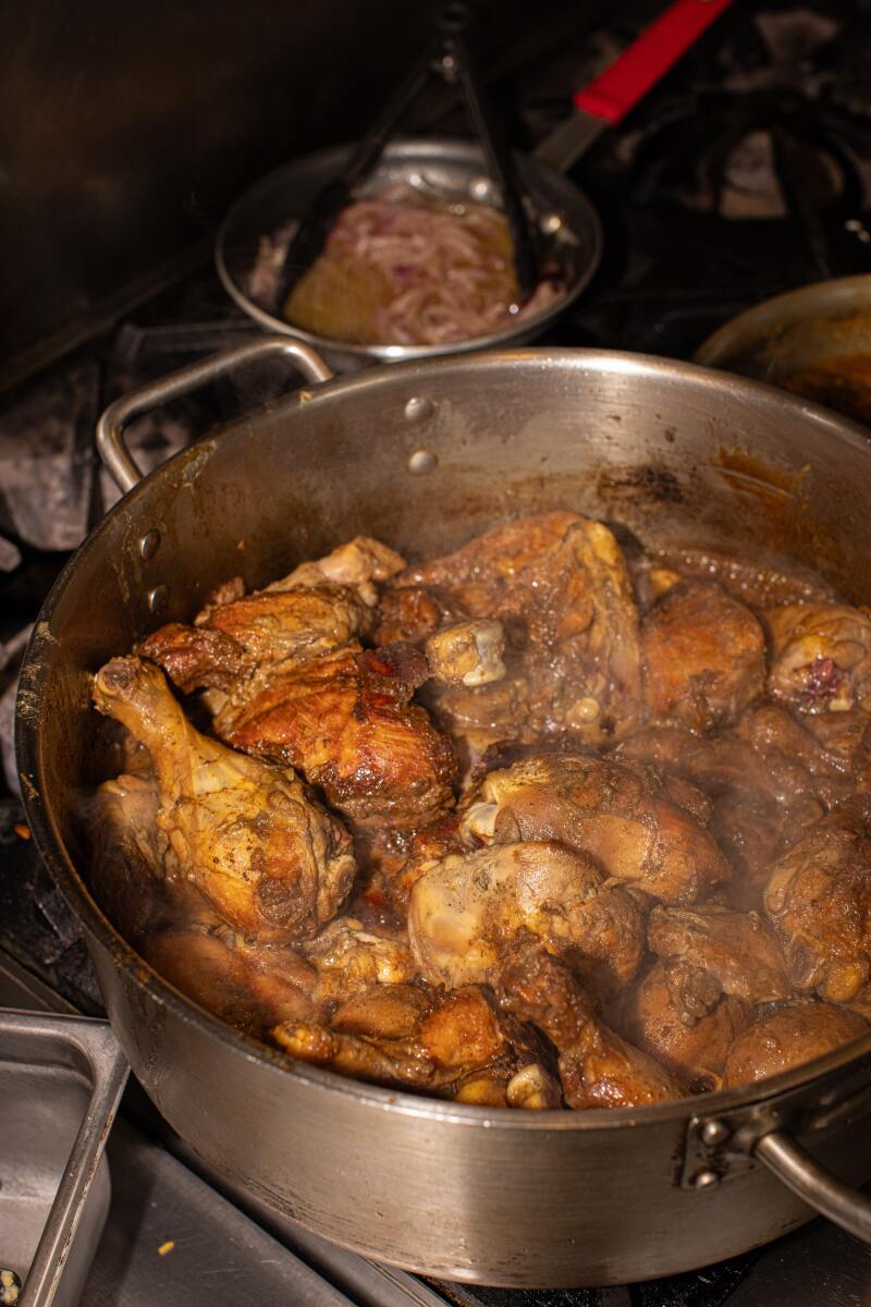 Eine Metallpfanne voller Hühnchen, das auf einem Restaurantherd kocht.  
