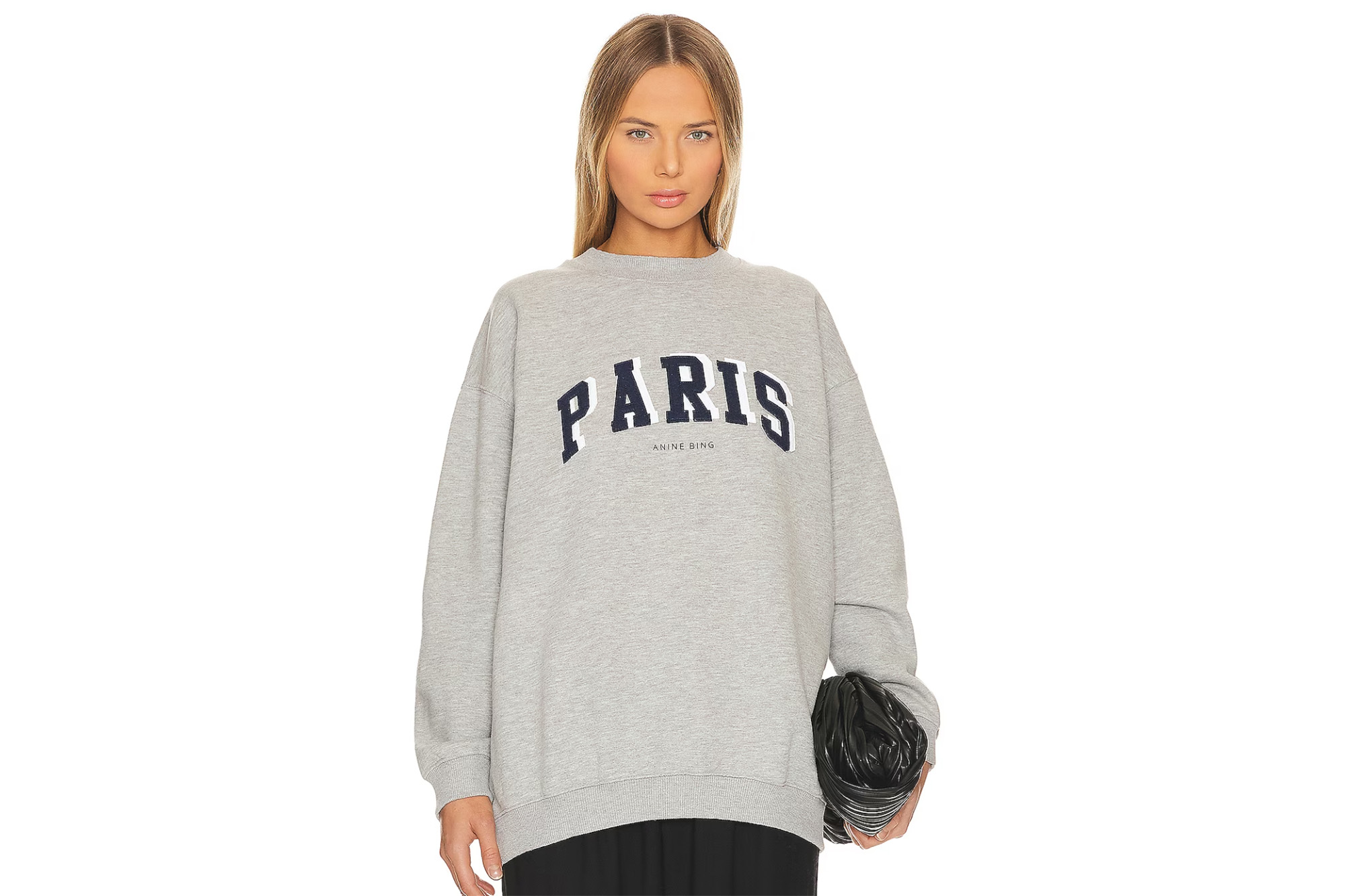 Ein Model in einem grauen Sweatshirt mit Rundhalsausschnitt, auf dem „Paris“ steht