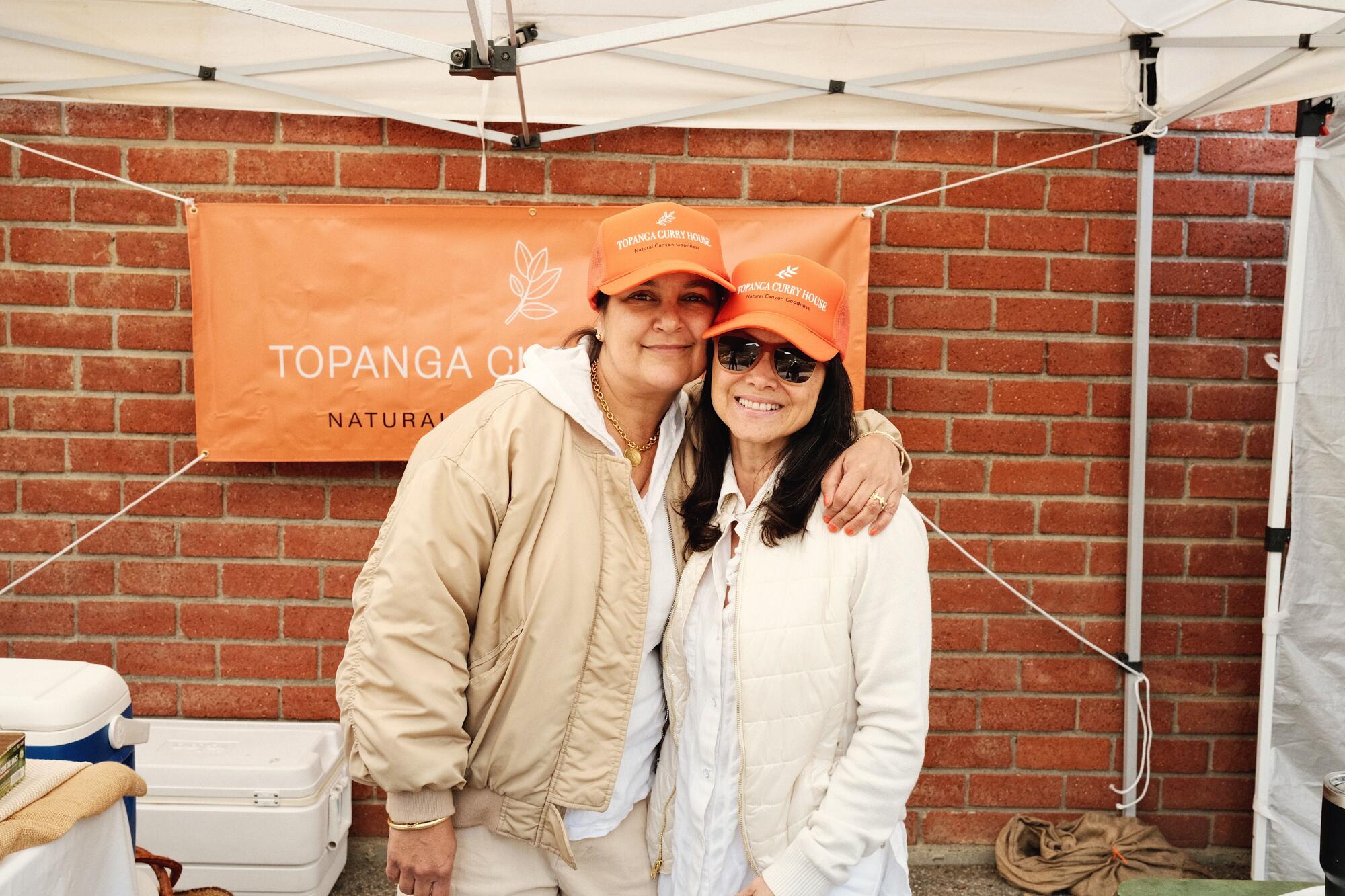 Claudia Joshi, links, mit einem Arm um Destiny London an ihrem orangefarbenen Stand im Topanga Curry House