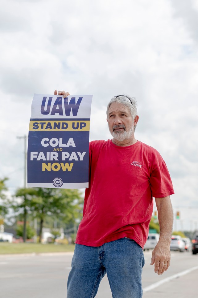Mann im roten Hemd hält ein UAW-Streikschild.