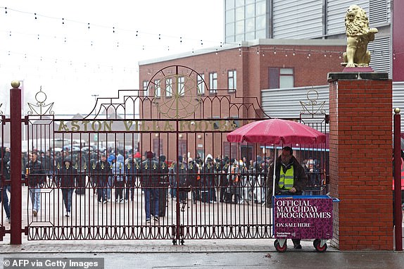 A programme seller shelters from the rain outside Villa Park in Birmingham, central England on March 10, 2024 ahead of the English Premier League football match between Aston Villa and Tottenham Hotspur. (Photo by Darren Staples / AFP) (Photo by DARREN STAPLES/AFP via Getty Images)