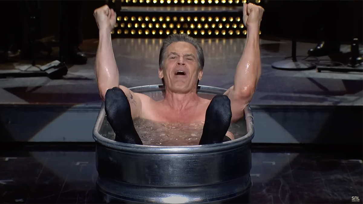 Josh Brolin in einer Wanne beim Kalttauchen am Set von "SNL" mit erhobenen Armen und ausgestreckten Füßen