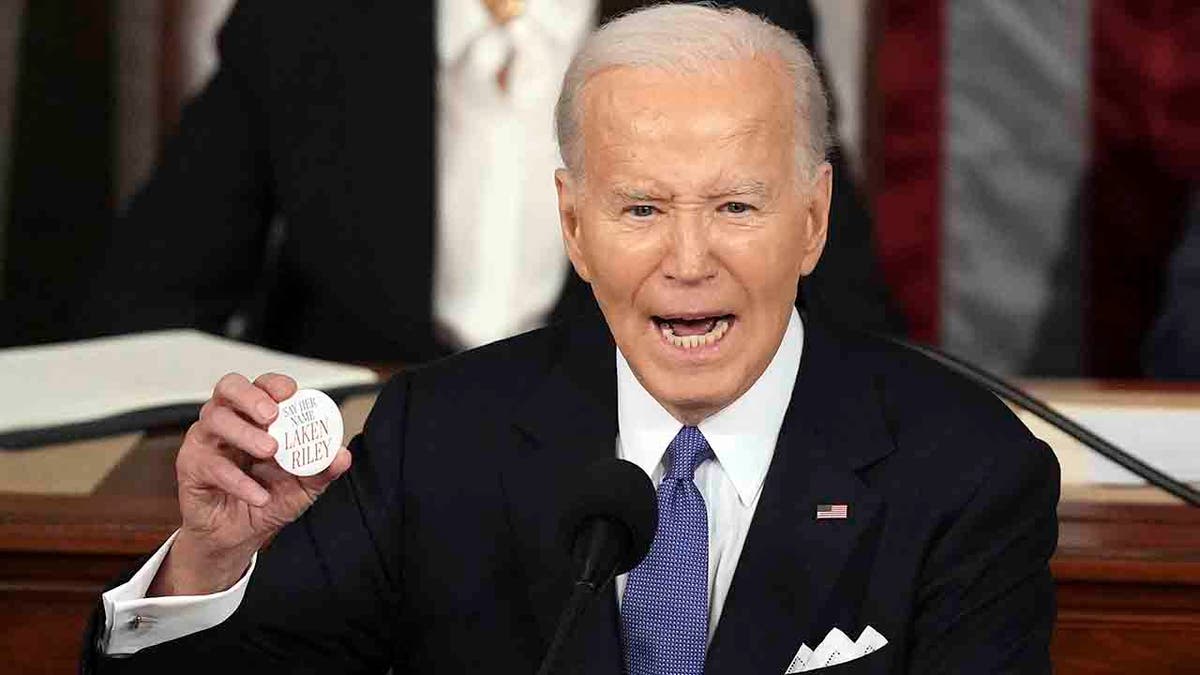 Präsident Joe Biden hält einen Laken-Riley-Knopf hoch