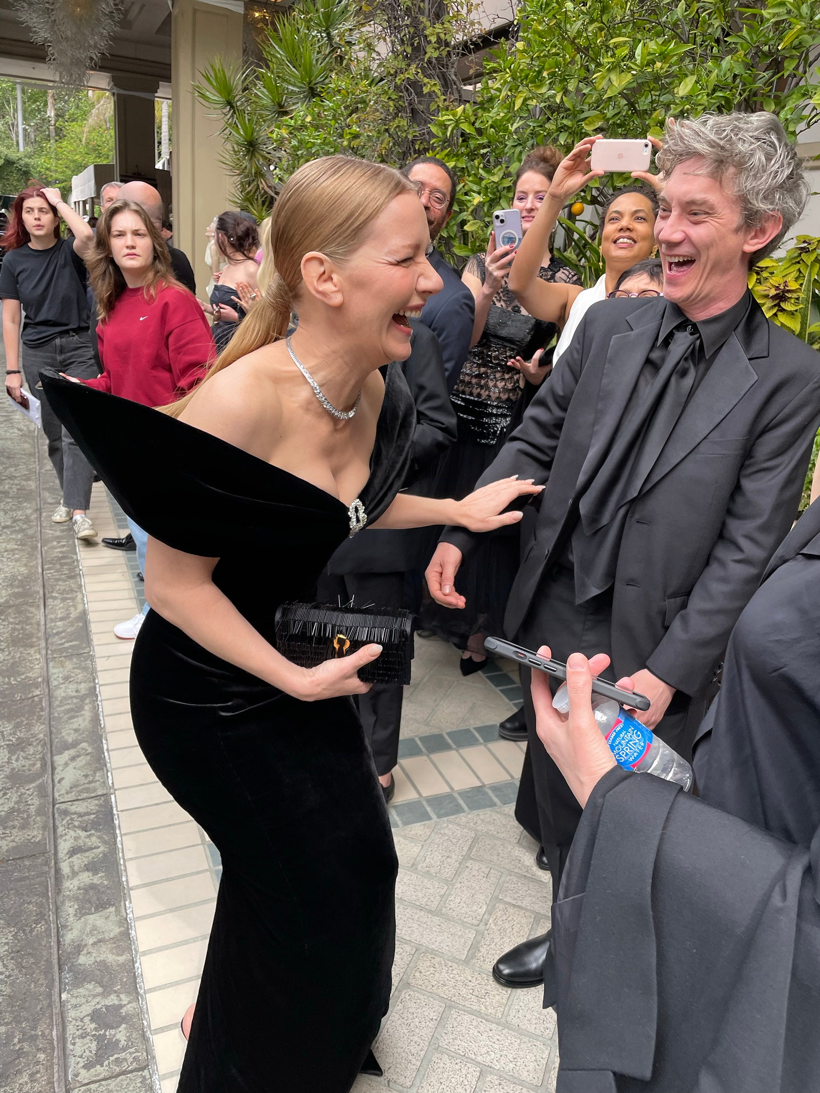 Sandra Hüller und Swann Arlaud lachen draußen, bevor sie zu den Oscars 2024 gehen.  Beide tragen ganz Schwarz.