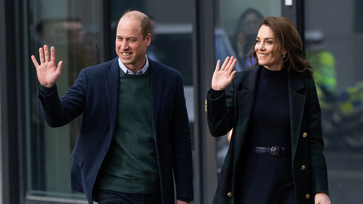 Prinz William in einem grünen Pullover und einem blauen Blazer winkt und geht neben Kate Middleton in einem grün-blauen Pullover-Blazer in Liverpool