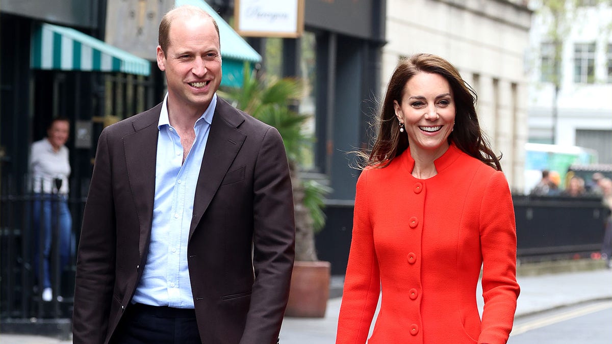 Prinz William lächelt, als er in einem roten Kleid neben Kate Middleton geht