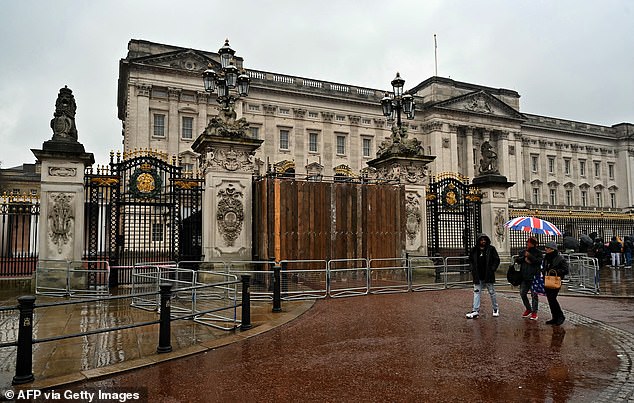 Menschen gehen am Sonntag an den mit Brettern vernagelten Toren vor dem Buckingham Palace in London vorbei