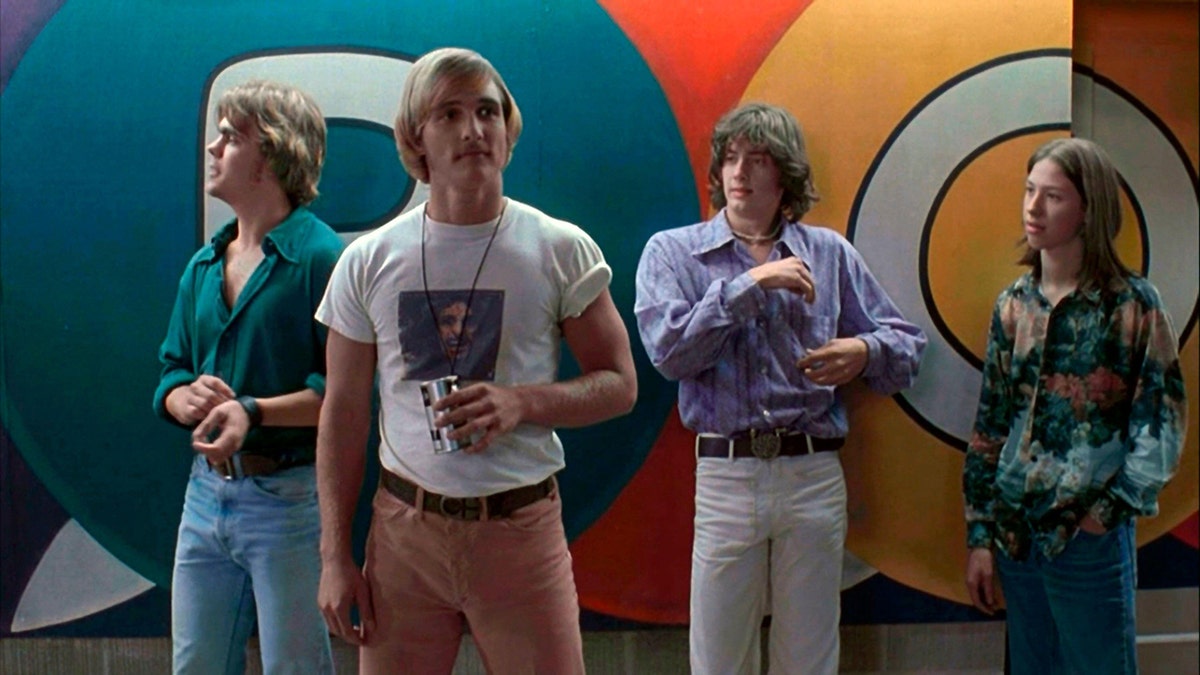 Matthew McConaughey in einem weißen T-Shirt und einer pfirsichfarbenen Hose in einer Szene aus "Benommen und verwirrt" steht mit anderen Jungs herum