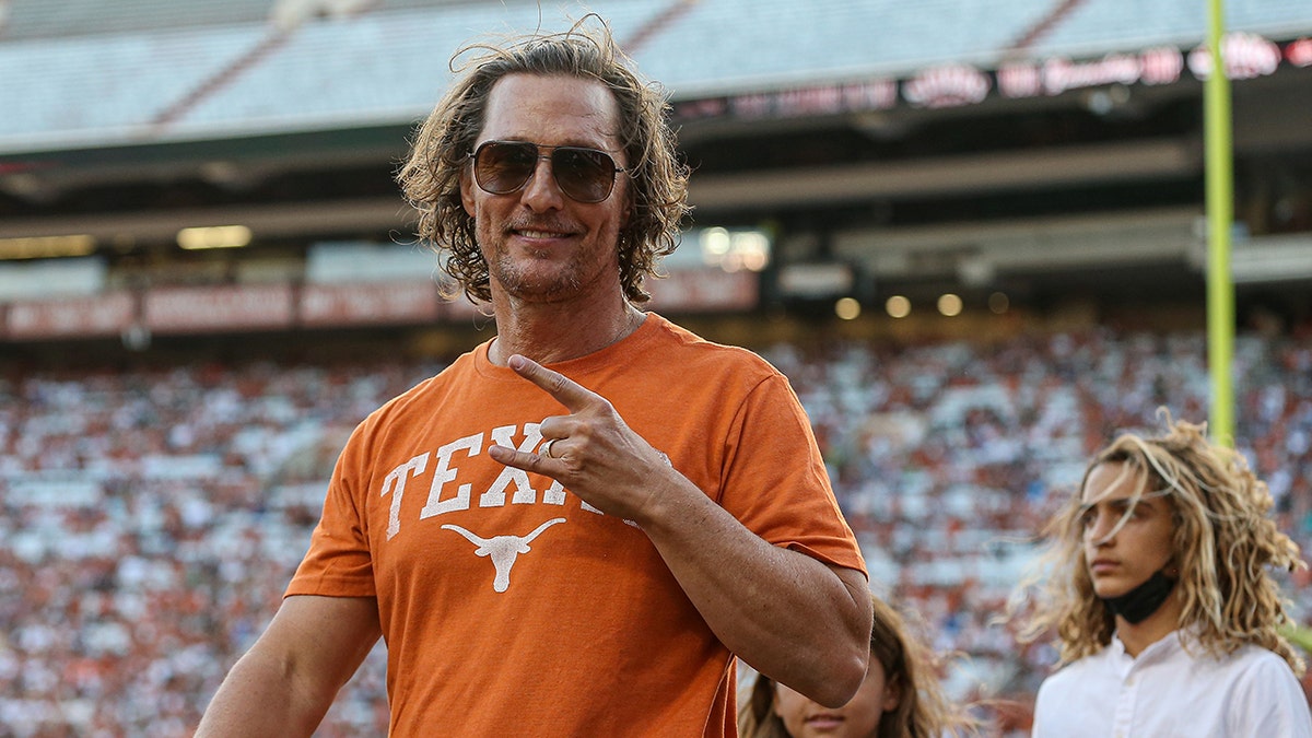 Matthew McConaughey trägt ein orangefarbenes Hemd mit der Aufschrift „Texas stellt das Friedenszeichen auf“.
