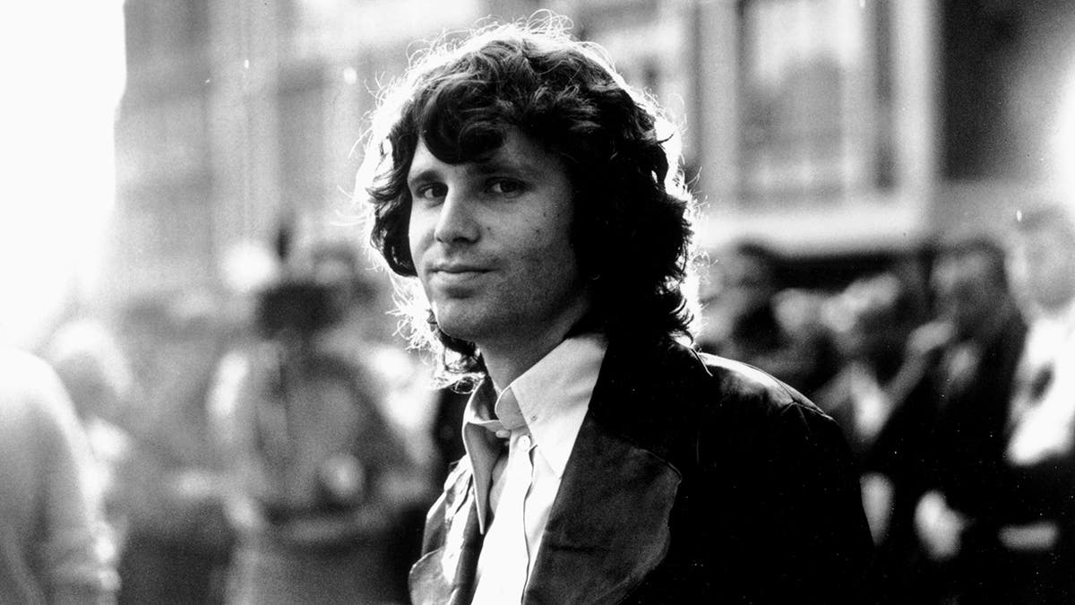 Schwarz-Weiß-Foto von Jim Morrison, der dezent in die Kamera grinst