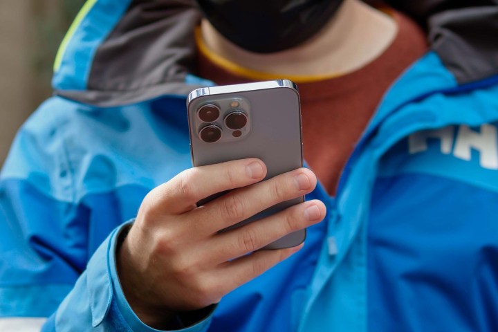 Man holding the iPhone 13 Pro showing its rear panel.
