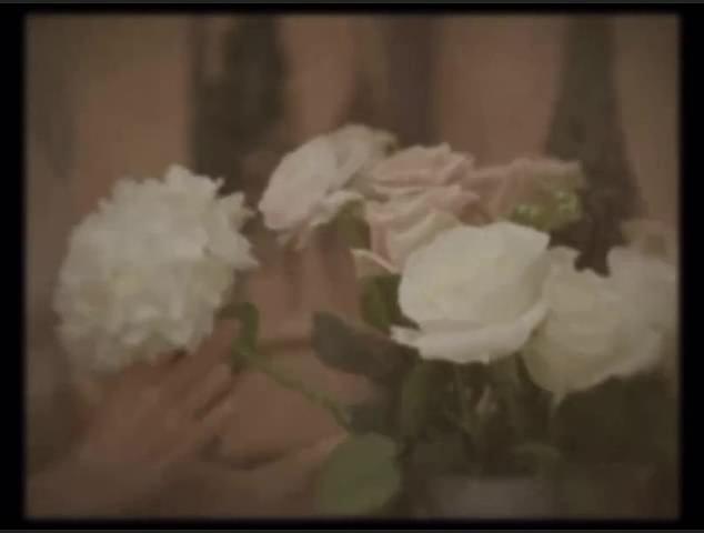 Das Video beginnt mit einem verwaschenen Video einer Frau, die weiße und rosa Pastellblumen arrangiert