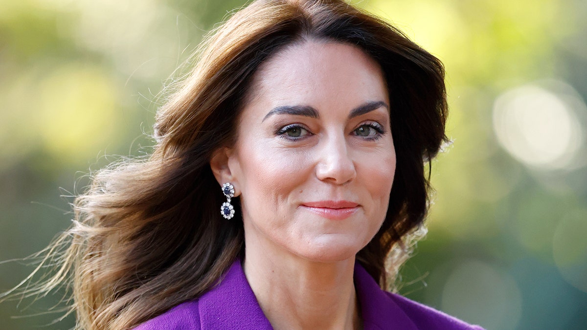 Kate Middleton grinst in einem lila Anzug