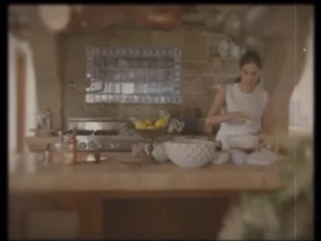 Dann wird ausgeblendet und zeigt Meghan, wie sie in einer atemberaubenden Küche kocht, über ihrem Kopf hängen Kupferpfannen, während sie rührt
