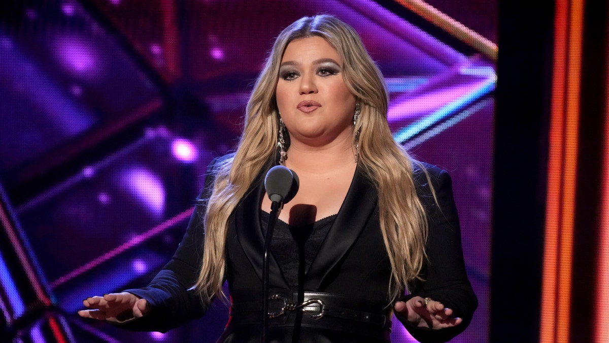 Kelly Clarkson in einem schwarzen Outfit hinter einem Mikrofon bei den iHeartRadio Music Awards