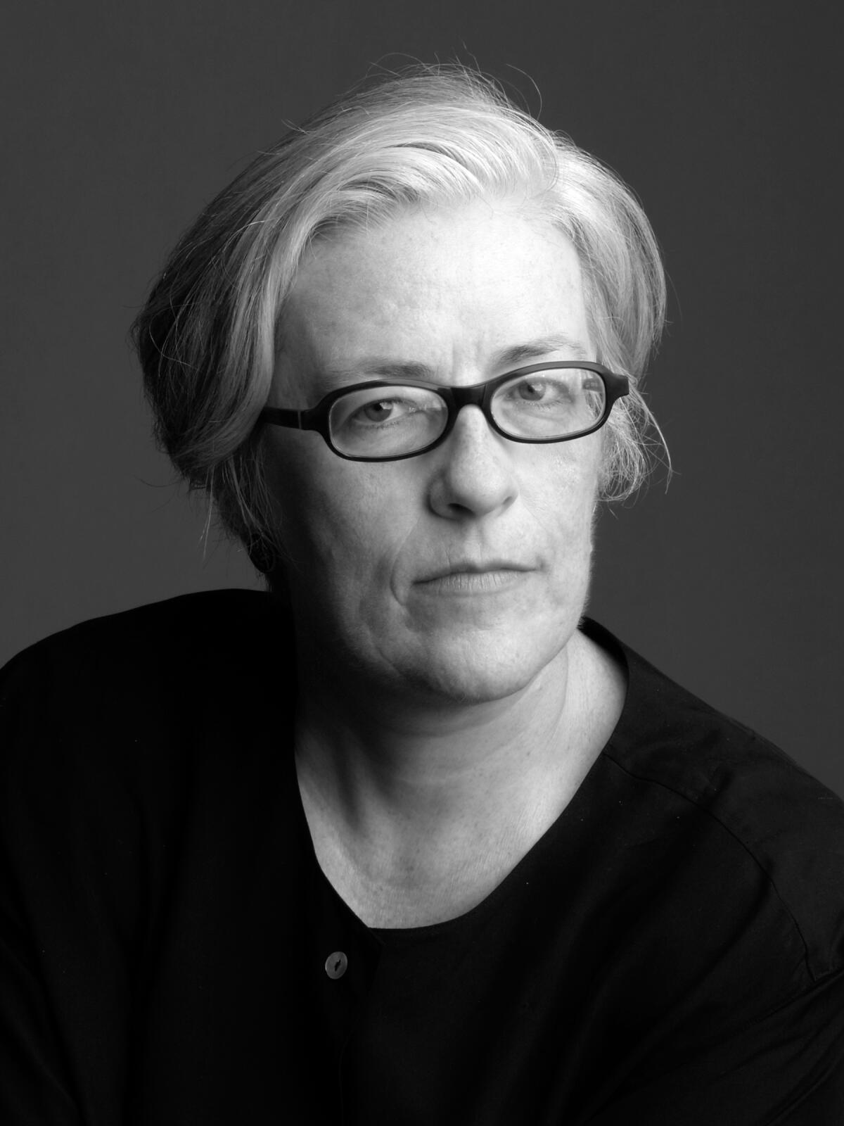 Ein Schwarz-Weiß-Kopffoto von Cynthia Carr mit kurzen Haaren, Brille und schwarzem Hemd.