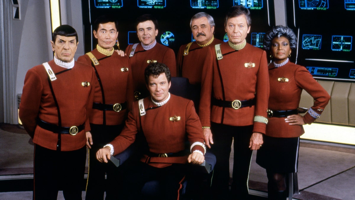 Leonard Nimoy, George Takei, Walter Koenig, DeForest Kelley, Nichelle Nichols und William Shatner, alle in roten Anzügen am Set von "Star Trek V: Die letzte Grenze"