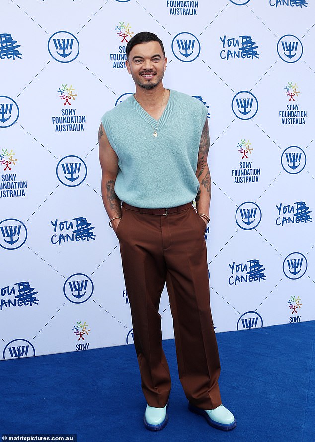 Guy Sebastian von The Voice zeigte seinen Bizeps in einer hellblauen Pulloverweste und einer braunen Hose, kombiniert mit klobigen blauen Stiefeln