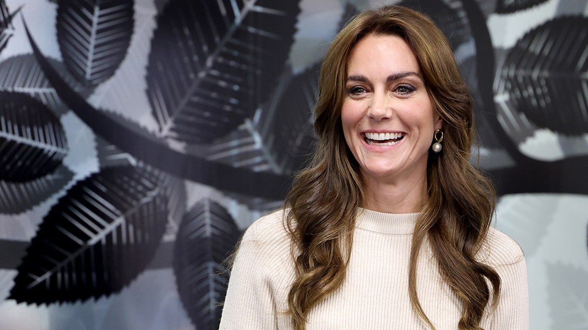 Kate Middleton in einem cremefarbenen Pullover lächelt