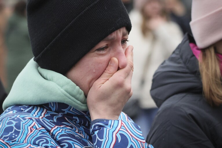 Eine Frau reagiert, als sie Blumen am Zaun neben dem Crocus-Rathaus am westlichen Rand von Moskau, Russland, am Sonntag, 24. März 2024, niederlegt. Der Moskauer Vorstadtkonzertsaal, in dem bewaffnete Männer das Feuer auf Konzertbesucher eröffneten, war ein geschwärztes, schwelende Ruine, als die Zahl der Todesopfer bei dem Angriff 130 überstieg und die russischen Behörden vier Verdächtige festnahmen.  (AP Photo/Vitaly Smolnikov)