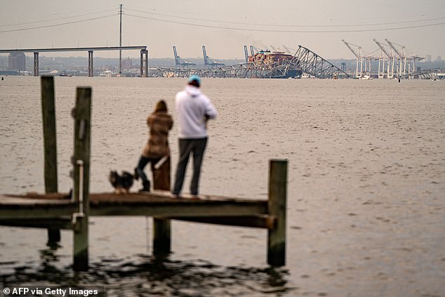 People look out toward the Francis Scott Key Bridge following its collapse after the Singapore-flagged Dali container ship collided with it along the Patapsco River on March 26