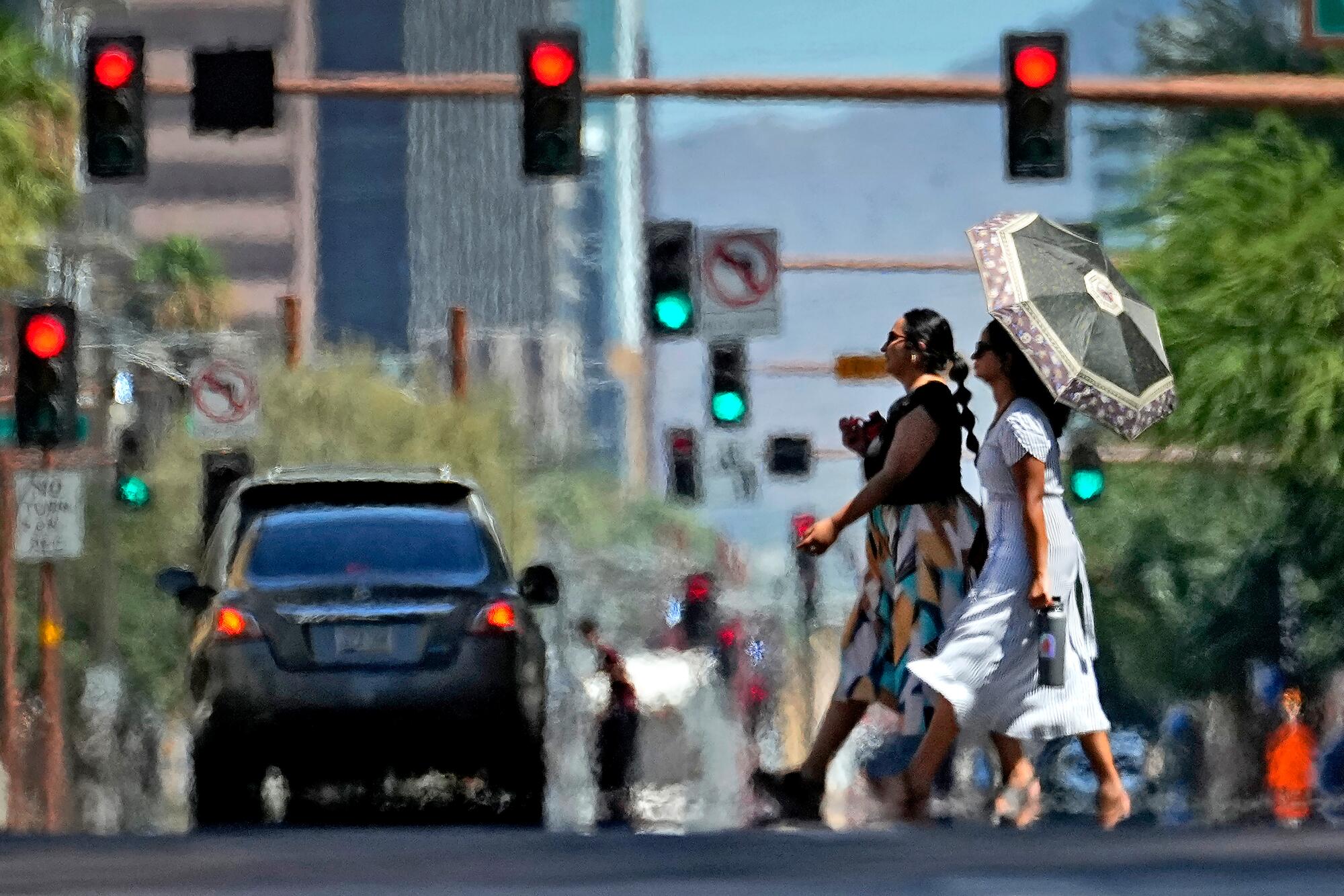 Hitzewellen breiten sich aus dem heißen Asphalt, als zwei Frauen eine Straße überqueren.